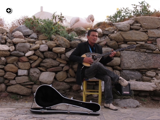 A bouzouki player entertains tourists in the Kastro area of Mykonos Town while one of the Mykonos pelicans preens behind him
