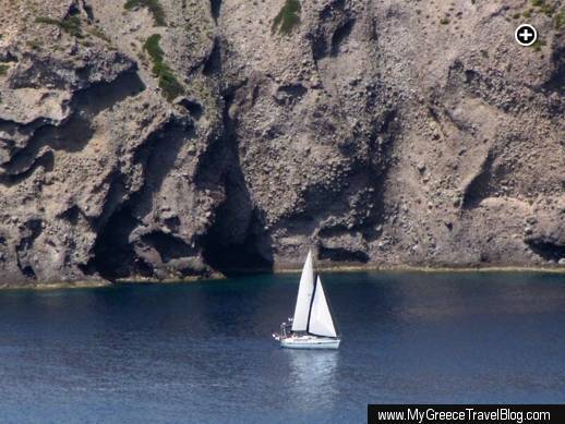 Rugged cliffs soar high above a sailboat passing the northwest coast of the Gulf of Milos
